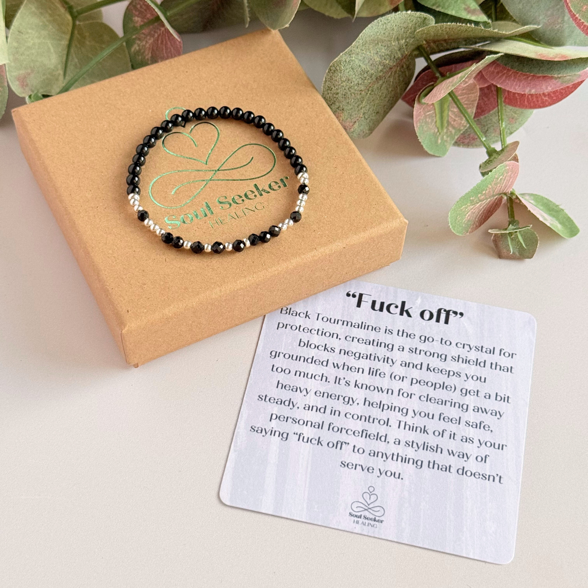 Elasticated black tourmaline crystal morse code bracelet spells out the words ‘Fuck off’ in a combination of 4mm round black tourmaline beads, 4mm faceted black tourmaline beads and either sterling silver or gold vermeil 3mm round beads. The words start and end at the rondelle spacer beads. Picture shows silver bracelet on top of the gift box with the crystal information card.